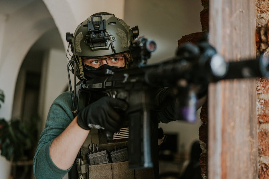 戦術装備を身に着けた兵士が屋内でライフルを構え、危険が迫る状況に集中して準備を整えている。