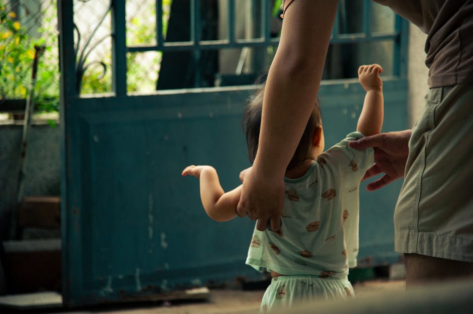 幼児が大人の支えを受けながら室内で歩くことを学ぶ、心温まる瞬間。