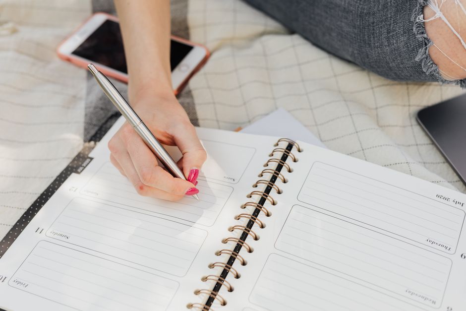 晴れた日に屋外でプランナーに書く女性。ライフスタイルや計画のテーマに最適です。