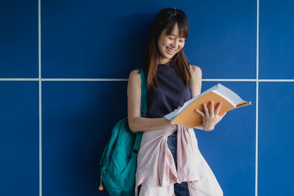 青い壁の近くで勉強しているワークブックを持つ幸せなアジアの女性