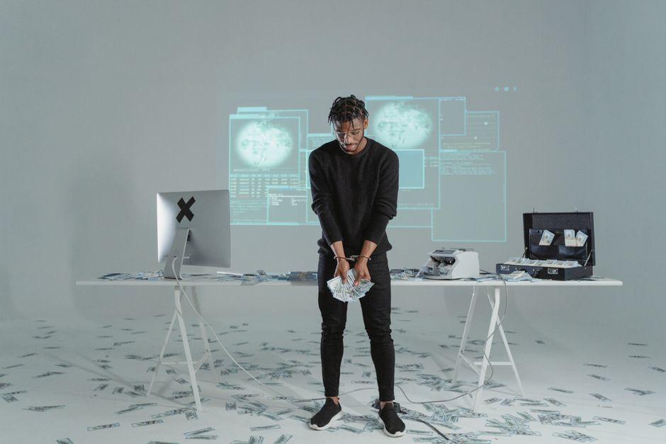 男性が散らばった札とコンピューターのセットアップがあるハイテクな部屋でお金を持っています。