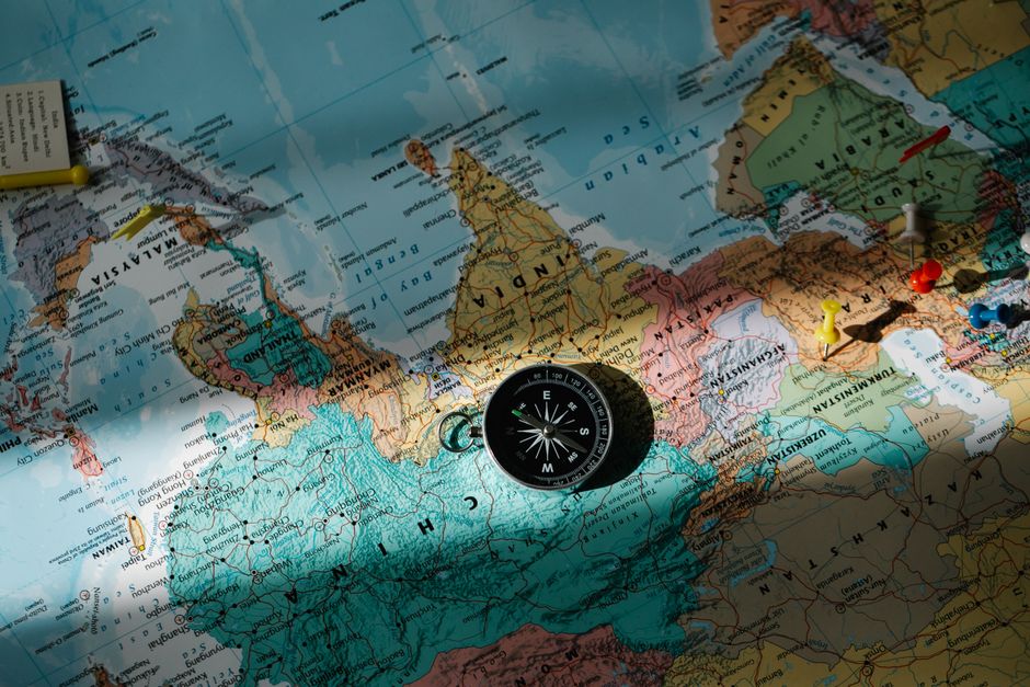 カラフルなピンが付いた詳細な世界地図の上に置かれたコンパス。