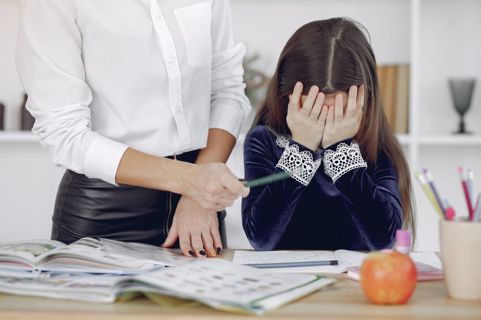 宿題に圧倒されている若い女の子と、屋内で彼女を助けている教師。