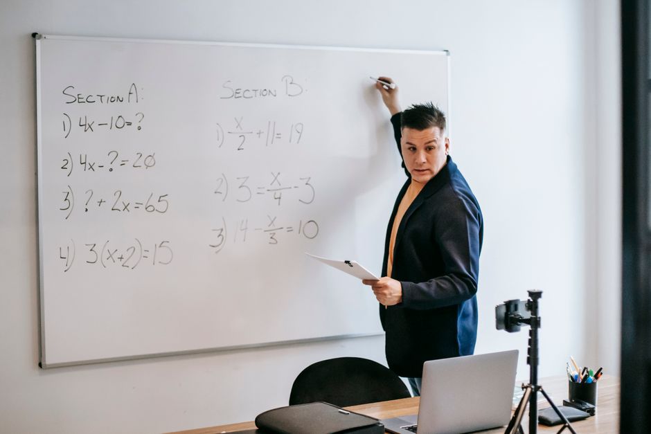 教師が現代の教室でホワイトボードに数学の問題を説明しています。