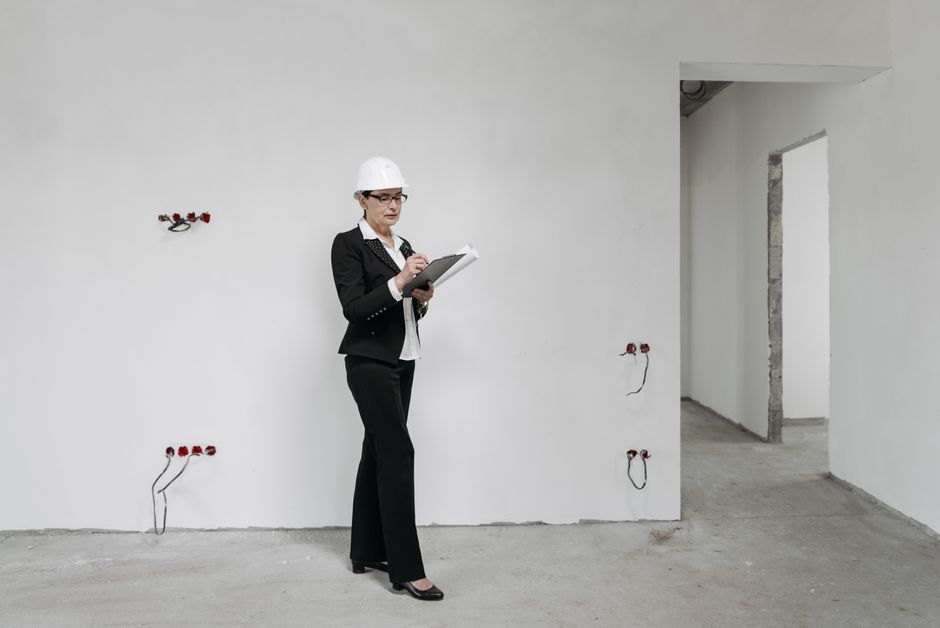 建設現場でヘルメットをかぶった女性がノートを確認し、進捗を調査しています。