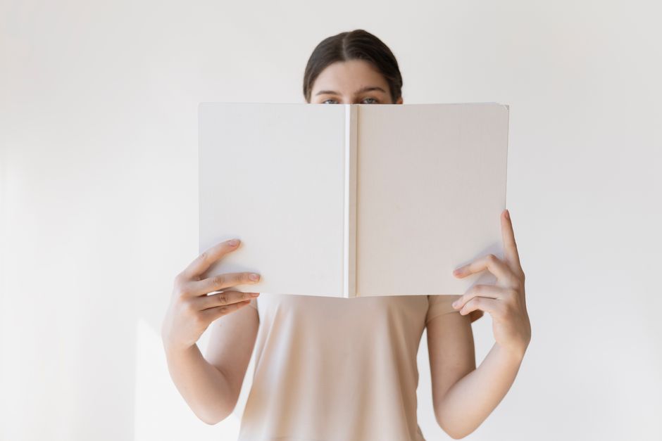 若い女性が顔の前で空白の本を持っており、モックアップの目的に最適です。