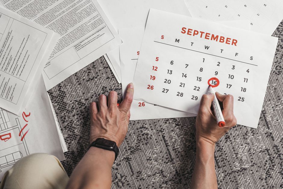 9月の日付が囲まれたカレンダーを持つ手と、カーペットの上の書類に囲まれています。